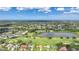 Aerial view of a lakeside home on a golf course, surrounded by lush greenery and neighboring houses at 1915 Pebble Beach Ct, Venice, FL 34293