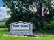 The Deep Creek deed restricted community sign adds charm to the neighborhood entrance, beneath mature trees and a waving American flag at 26090 Rampart Blvd, Punta Gorda, FL 33983