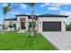 Beautiful modern home with manicured lawn, palm trees, a dark gray garage door and a light gray brick driveway at 14166 Fort Worth Cir, Port Charlotte, FL 33981