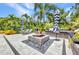 Outdoor stone patio with a cozy fire pit, lounge chairs, and bench seating surrounded by lush tropical landscaping at 25062 Palisade Rd, Punta Gorda, FL 33983