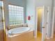 Bright bathroom features a soaking tub with tile surround and a unique glass block window at 421 Marsh Creek Rd, Venice, FL 34292