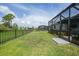View of backyard with a screened-in lanai, black metal fence and plush green grass at 11383 Burgundy Dr, Venice, FL 34293