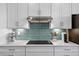 Close up of a cooktop and backsplash in a modern kitchen with white cabinets and stainless steel appliances at 17336 Sandpearl Rd, Venice, FL 34293