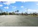 A full outdoor tennis court with fencing, overhead lighting, and palm tree landscaping near parking areas at 17336 Sandpearl Rd, Venice, FL 34293