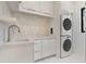Bright laundry room features stackable washer and dryer, sleek white cabinets, and modern tile backsplash at 245 Lido Dr, Punta Gorda, FL 33950