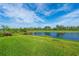 Scenic view of a pond surrounded by a well-manicured green lawn and lush trees under a bright sky at 14846 Contenta Loop, Bradenton, FL 34211