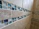 Close-up of a shower with beige stone and blue glass tile details at 8025 Weyers Ct, Englewood, FL 34224
