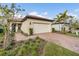 Beige house with a white garage door, palm trees, and a brick paved walkway at 2759 Lavandula Ct, North Port, FL 34289