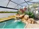 Screened in pool featuring rock waterfall and lush tropical landscaping, overlooking the water view at 170 Antilla Dr, Rotonda West, FL 33947