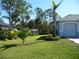 Well-maintained lawn, mature trees, and a glimpse of the light-blue home with a manicured garden bed at 380 Hoffer St, Port Charlotte, FL 33953