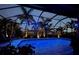 Screened-in pool with lights, palm trees, and view of a two-story house at night at 214 W Pine Valley Ln, Rotonda West, FL 33947