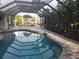 Enclosed pool area with grey brick floor, filled pool, tropical garden, and metal screening at 232 Bahia Vista Dr, Englewood, FL 34223