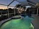 An evening view of a screened pool and hot tub, illuminated and with views of the waterway at 2160 Palm Tree Dr, Punta Gorda, FL 33950