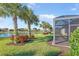 Scenic backyard with a screened-in lanai, tropical palm trees, vibrant plants, and a peaceful lake view at 19241 Serafina St, Venice, FL 34293