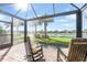 Relaxing screened-in lanai with brick floor and rocking chairs overlooks a serene lake and tropical landscaping at 19241 Serafina St, Venice, FL 34293