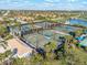 Aerial view showcasing multiple tennis courts with blue canopies, lush landscaping, and nearby lake at 19241 Serafina St, Venice, FL 34293