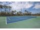 Outdoor tennis court with blue and green surface, surrounded by tall trees and fencing at 10310 Coral Landings Ct # 98, Placida, FL 33946