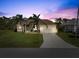 Charming single-story home with a well-manicured lawn and two-car garage, framed by mature palm trees at dusk at 127 White Marsh Ln, Rotonda West, FL 33947
