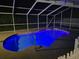 Night view of a kidney-shaped pool with screen enclosure and illuminated blue water, creating a tranquil ambiance at 10075 Bay Ave, Englewood, FL 34224