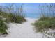 Sandy path leading to a serene beach with calm, turquoise waters, framed by natural dune vegetation at 108 Fairway Rd, Rotonda West, FL 33947