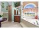 Elegant primary bathroom featuring tiled shower, granite counters, and soaking tub with arched window overlooking a yard at 103 Mecca St, Port Charlotte, FL 33954