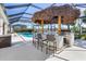 Outdoor kitchen with granite countertops and bar seating with pool in the background at 14564 Gaspar Loop, Port Charlotte, FL 33981