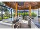 An outdoor kitchen with stainless steel appliances, a covered tiki bar, and a view of the lush backyard at 14564 Gaspar Loop, Port Charlotte, FL 33981