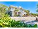 Two-story coastal home with white exterior, palm trees, large yard with rock groundcover and stairway to the front door at 62 Tarpon Way, Placida, FL 33946