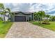 Home's exterior features a paver driveway, lush lawn, mature palm trees, and a attached two-car garage, creating an inviting curb appeal at 8304 Antwerp Cir, Port Charlotte, FL 33981