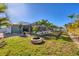 Expansive backyard featuring a lush green lawn, stone fire pit, palm trees, white fence, and a screened-in pool area at 10039 Sunday Dr, Port Charlotte, FL 33981