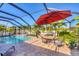 Inviting screened-in pool area features an umbrella-covered dining table and comfortable outdoor seating for entertaining guests at 10039 Sunday Dr, Port Charlotte, FL 33981