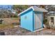 A bright blue shed in the yard, featuring a silver sun decoration, white double doors, and a gray roof at 7035 Duke St, Englewood, FL 34224