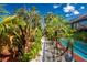 Beautiful backyard pathway bordered by tropical plants, leading to a screened pool area with water views at 1670 Faust Dr, Englewood, FL 34224