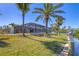 Exterior view showcasing a screened-in pool, lush lawn, palm trees, and dock on the waterfront at 30 Buccaneer Bnd, Placida, FL 33946