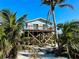 Charming coastal home on stilts with light blue siding and a cozy balcony, surrounded by lush tropical vegetation at 8714 King St, Placida, FL 33946