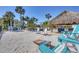 Sandy backyard beach area with a tiki hut, Adirondack chairs, and a cornhole game set at 10500 Sherman St, Englewood, FL 34224