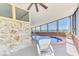 Serene indoor pool area with stunning waterfront views, complemented by stylish stone accent wall and lounge chair at 6029 Manasota Key Rd, Englewood, FL 34223