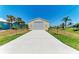 Detached, neutral garage with large driveway surrounded by vibrant green grass, palm trees, and clear blue skies at 9404 Arnaz Cir, Port Charlotte, FL 33981