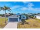 Exterior elevation of a one-story light blue home featuring a two-car garage, palm tree, and a well-manicured lawn at 12359 Deepwoods Ave, Port Charlotte, FL 33981
