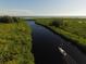 Picturesque aerial view of a sailboat on a scenic canal with lush greenery and calm waters under a clear blue sky at 15092 Chinook Way, Port Charlotte, FL 33981