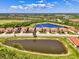 Wide aerial shot featuring a row of homes with red tile roofs, situated near a lake and surrounded by mature trees at 23590 Copperleaf Dr, Venice, FL 34293