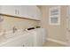 Well-lit laundry room featuring white cabinets, sink, washer, dryer, and window at 23590 Copperleaf Dr, Venice, FL 34293