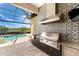 A stainless steel outdoor kitchen including a grill, fridge, sink, and patterned backsplash at 257 Corelli Dr, Nokomis, FL 34275
