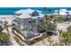 A stunning two-story beach house boasts detailed latticework, a pristine white staircase, and lush tropical landscaping at 6890 Palm Island Dr, Placida, FL 33946