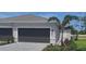 Exterior view of home featuring a gray two car garage, manicured landscaping, and a charming palm tree at 8661 Seasalt Loop, Englewood, FL 34224