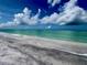 Gentle waves lap onto a pristine white sand beach with clear turquoise water under a bright blue sky with fluffy white clouds at 9594 Doubloon Trl, Placida, FL 33946