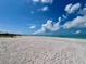 Expansive white sand beach meets clear turquoise water under a bright blue sky with fluffy white clouds at 9594 Doubloon Trl, Placida, FL 33946