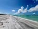 The clear turquoise water meets a pristine white sand beach under a bright blue sky with fluffy white clouds at 9594 Doubloon Trl, Placida, FL 33946