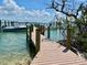 View of a wooden dock leading to a tranquil marina with boats and clear turquoise water under a bright blue sky at 9594 Doubloon Trl, Placida, FL 33946