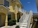 Two-story yellow home featuring outdoor staircase with white railing and well-maintained landscaping at 169 Boundary Blvd # 169P, Rotonda West, FL 33947